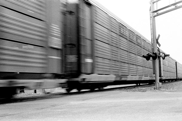 Metal Art Print - A blurred motion photograph of a train at a railroad crossing.